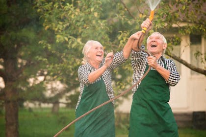 Pensjonister i hagen som ler mens de holder en hageslange i mellom seg. Foto
