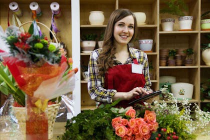 Kvinne står og smiler i sin egen butikk for blomster. Foto