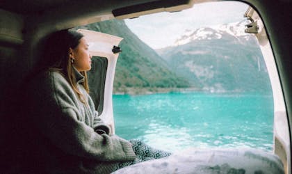 Kvinne sit i ein bil og ser utover eit fjellvatn. Foto