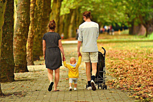 Mann, kvinne og barn går tur i parken blant trær. Foto