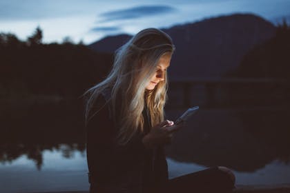 Kvinne står ute en mørk kveld med mobil i hendene. Foto